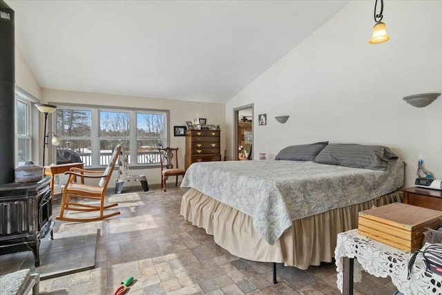 bedroom featuring lofted ceiling, stone finish floor, and a wood stove