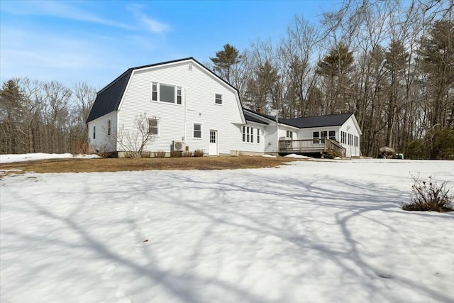 view of snow covered exterior with a wooden deck and a gambrel roof