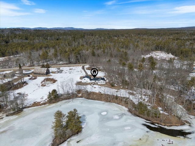 snowy aerial view featuring a mountain view and a wooded view