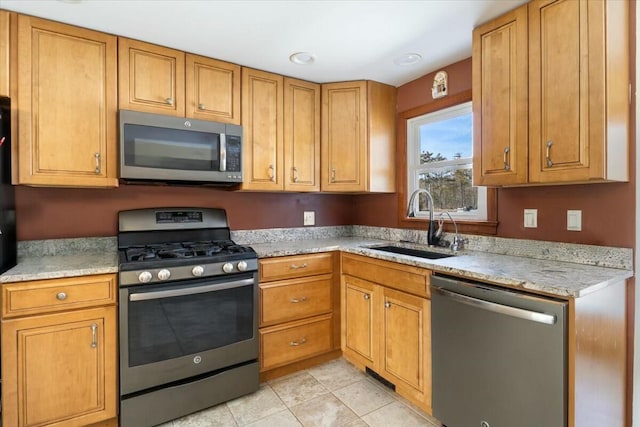 kitchen with light tile patterned floors, appliances with stainless steel finishes, brown cabinetry, and a sink