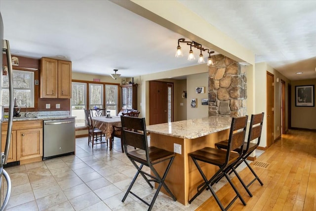 kitchen featuring light stone counters, a peninsula, a kitchen breakfast bar, and stainless steel dishwasher