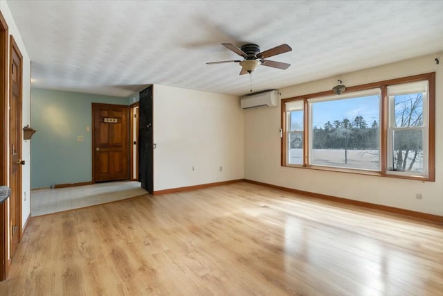 spare room featuring light wood-style flooring, a ceiling fan, baseboards, and a wall mounted AC