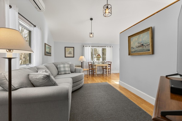 living room featuring a wall unit AC, light hardwood / wood-style floors, and vaulted ceiling