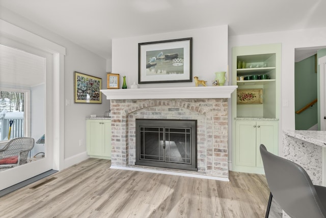 living room featuring built in shelves, a brick fireplace, and light hardwood / wood-style flooring