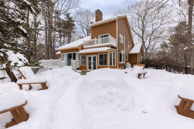 snow covered back of property featuring french doors and a balcony