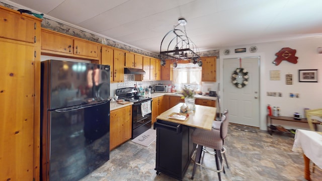 kitchen featuring brown cabinets, under cabinet range hood, light countertops, black appliances, and a chandelier