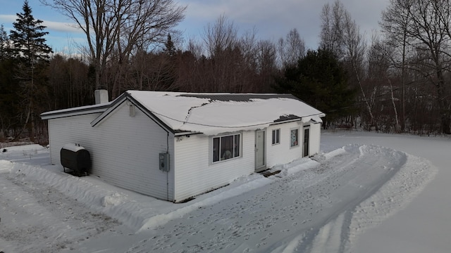 snow covered property with a forest view, heating fuel, and a chimney