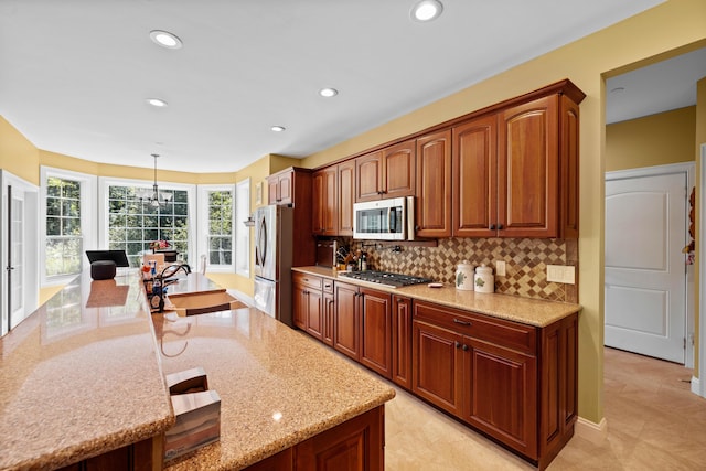 kitchen featuring sink, stainless steel appliances, light stone counters, tasteful backsplash, and decorative light fixtures