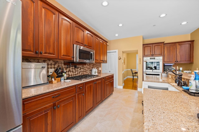 kitchen with stainless steel appliances, light stone countertops, sink, and decorative backsplash