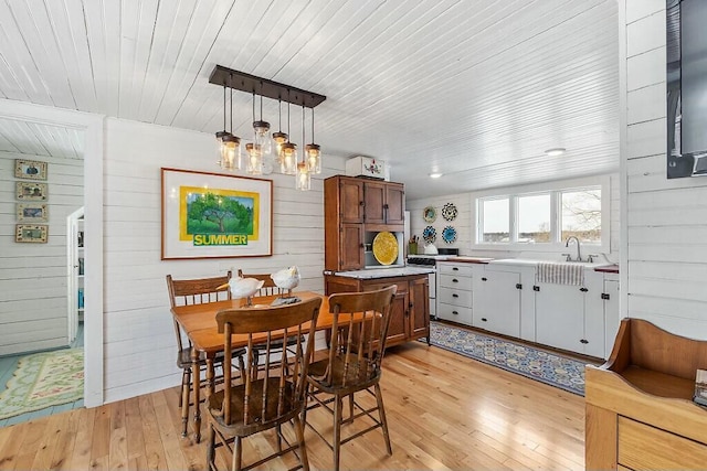 dining area with light wood-type flooring, wooden ceiling, and wood walls