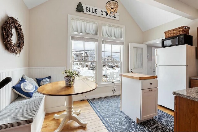 dining room featuring lofted ceiling, light wood-style flooring, breakfast area, and wainscoting