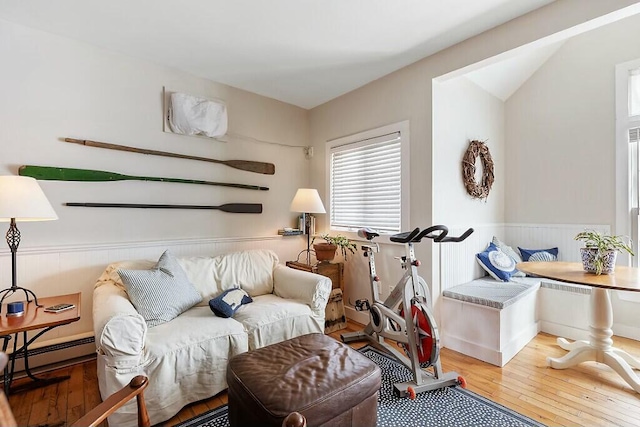 living area with a wainscoted wall, a baseboard heating unit, and wood-type flooring