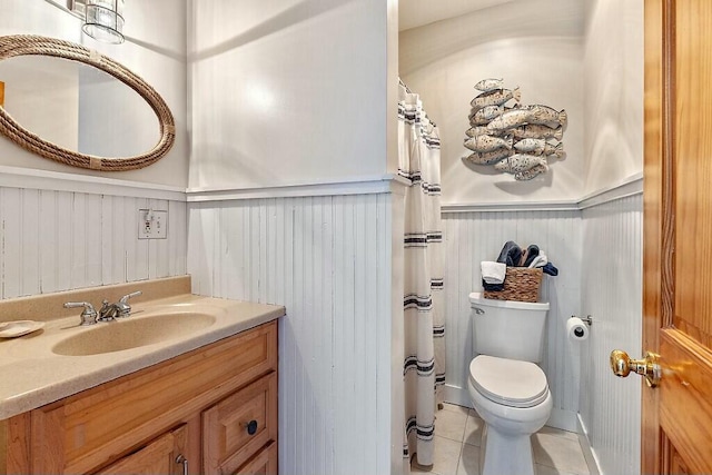 bathroom with curtained shower, toilet, vanity, wainscoting, and tile patterned floors