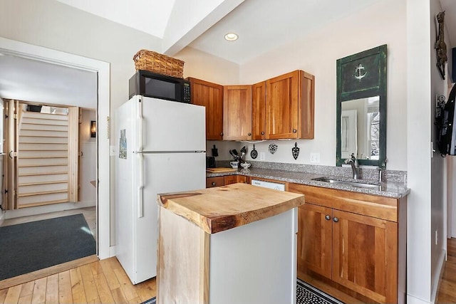 kitchen featuring white appliances, light wood finished floors, a kitchen island, brown cabinets, and a sink