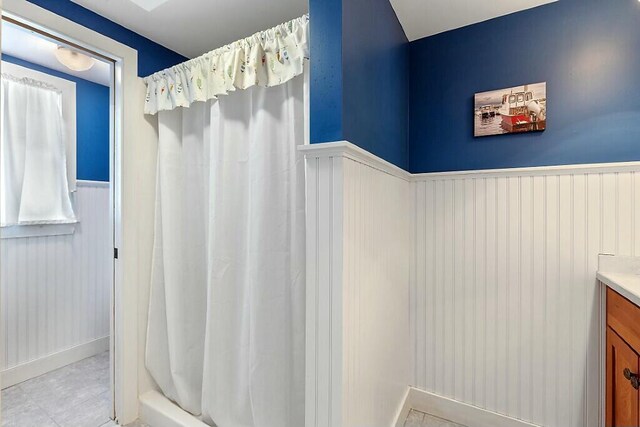 bathroom featuring a wainscoted wall, curtained shower, and vanity