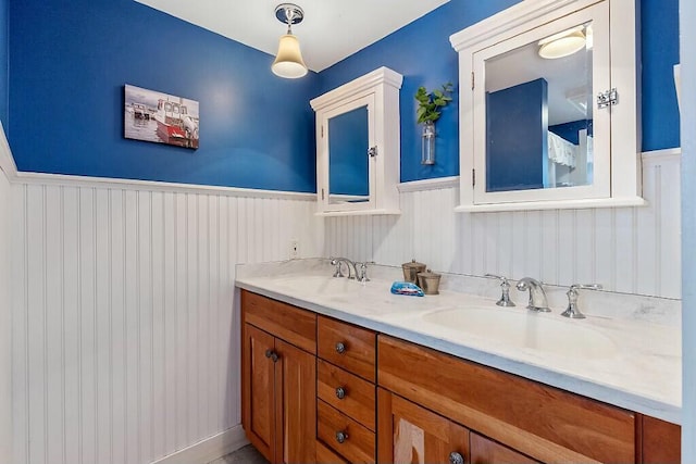 full bathroom featuring double vanity, a wainscoted wall, and a sink