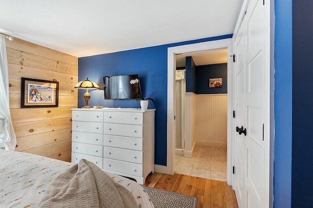 bedroom with wood walls, wood finished floors, and a wainscoted wall