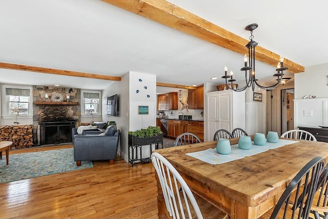 dining area with light wood-style floors, a fireplace, a chandelier, and beam ceiling