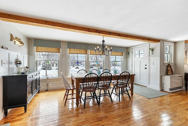 dining area featuring light wood finished floors, an inviting chandelier, beamed ceiling, and wainscoting