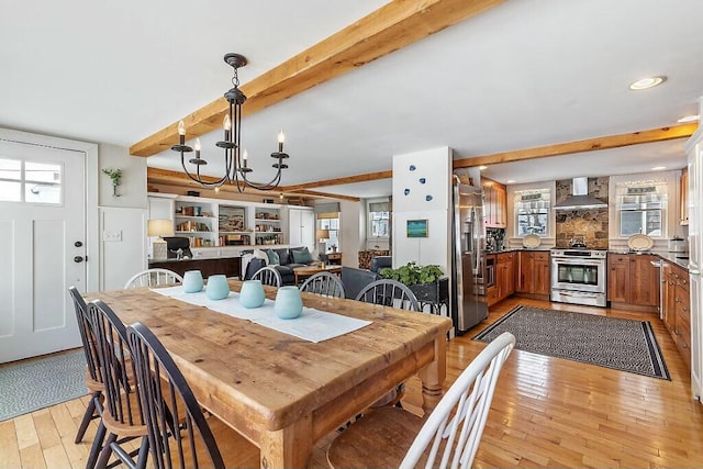 dining space with light wood finished floors, plenty of natural light, beam ceiling, and an inviting chandelier