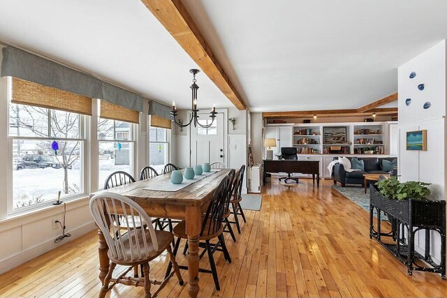 dining space featuring a notable chandelier, light wood-style flooring, a decorative wall, and beamed ceiling