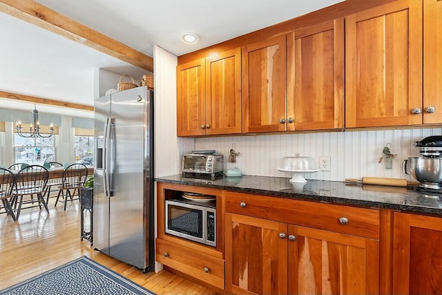 kitchen featuring light wood-style flooring, appliances with stainless steel finishes, brown cabinetry, and dark stone counters