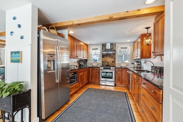 kitchen with a sink, appliances with stainless steel finishes, brown cabinets, wall chimney exhaust hood, and light wood finished floors