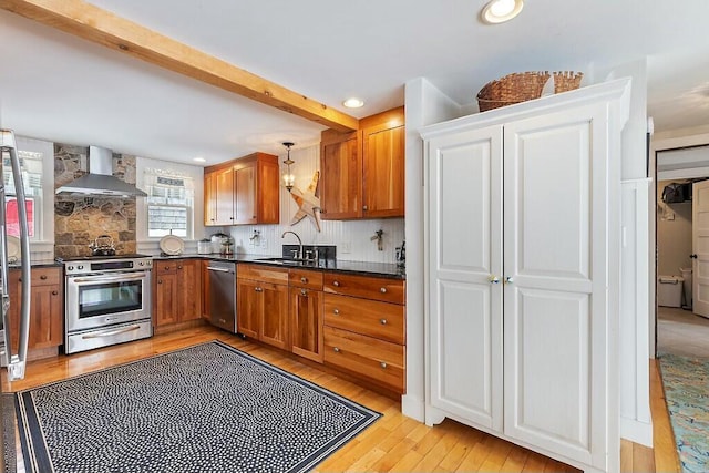 kitchen featuring wall chimney exhaust hood, appliances with stainless steel finishes, brown cabinetry, and a sink