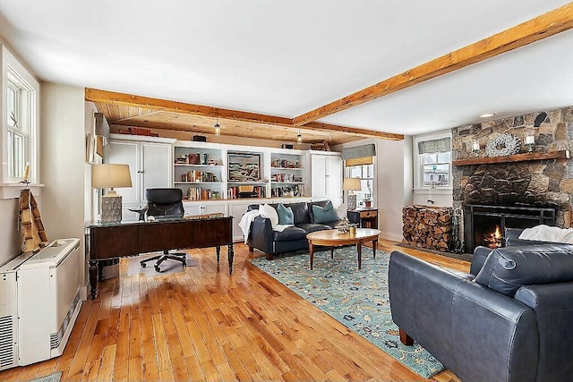 living room with a stone fireplace, beamed ceiling, and hardwood / wood-style floors