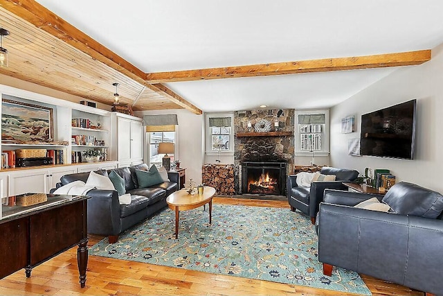 living room with beamed ceiling, hardwood / wood-style floors, and a stone fireplace