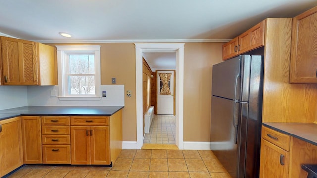 kitchen featuring dark countertops, light tile patterned flooring, brown cabinets, and freestanding refrigerator