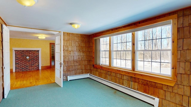 carpeted spare room with wood walls, french doors, and a baseboard radiator