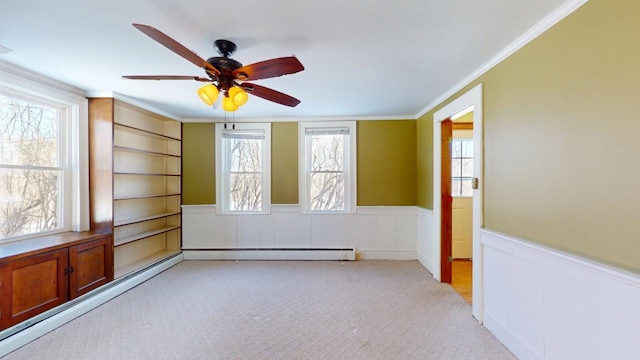 empty room with light colored carpet, a wainscoted wall, baseboard heating, and ornamental molding