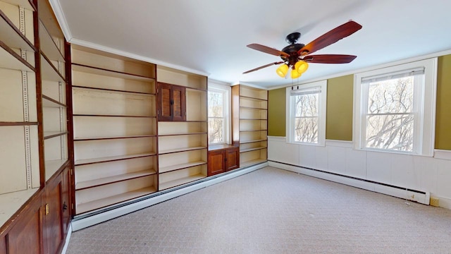 spare room featuring a baseboard heating unit, crown molding, a ceiling fan, and wainscoting