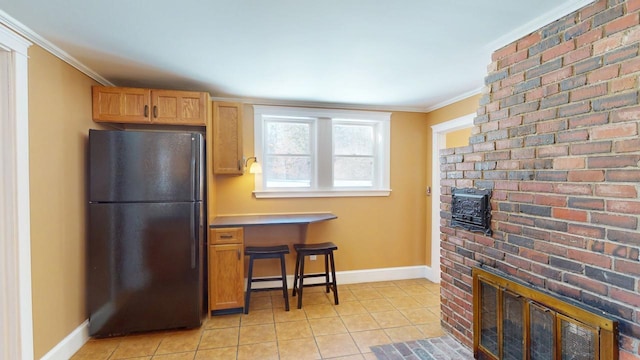 kitchen with light tile patterned floors, crown molding, freestanding refrigerator, and baseboards