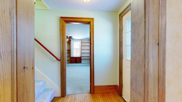 corridor featuring baseboards, stairs, and light wood finished floors