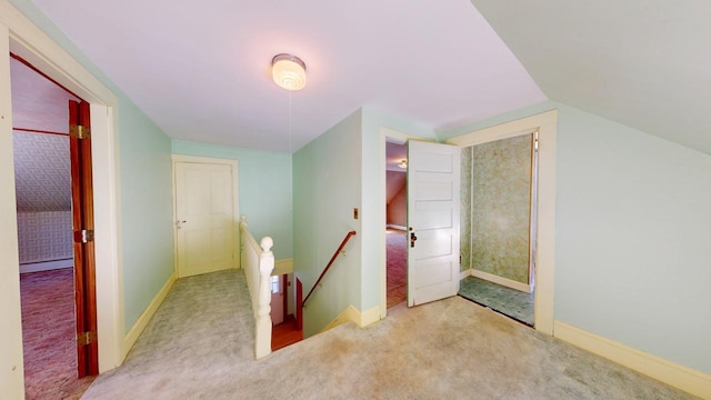 hall with an upstairs landing, lofted ceiling, carpet, a baseboard radiator, and baseboards