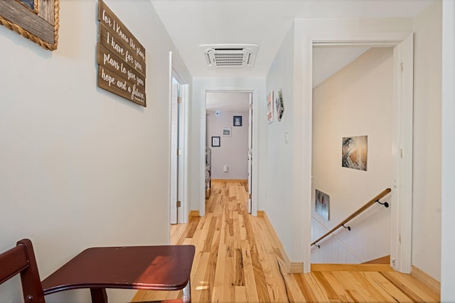 hall featuring baseboards, visible vents, an upstairs landing, and wood finished floors