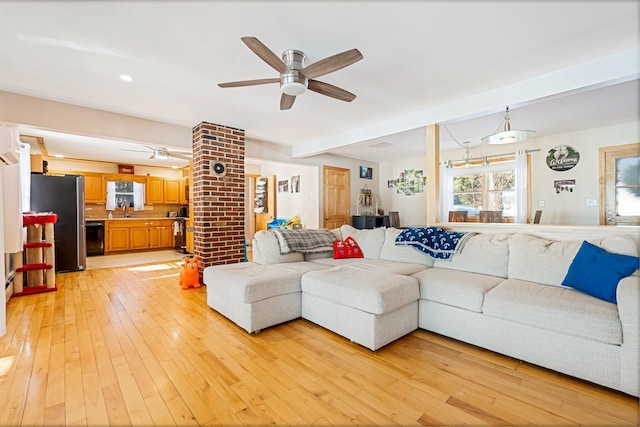 living area with beam ceiling, ceiling fan, and light wood finished floors