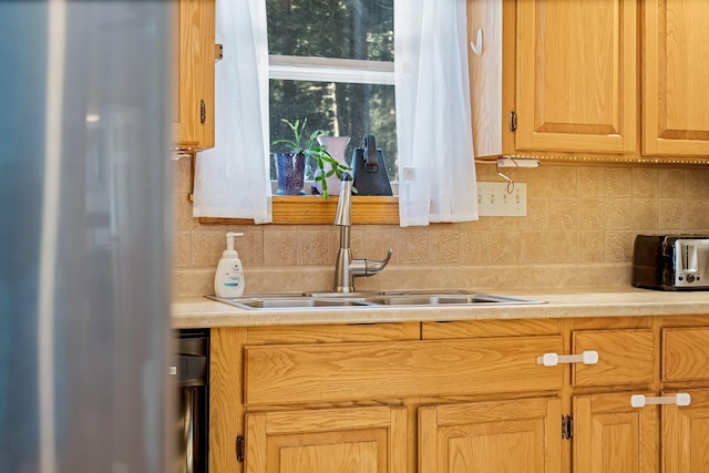 kitchen featuring a toaster, decorative backsplash, refrigerator, light countertops, and a sink