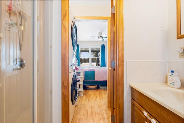 ensuite bathroom with a ceiling fan, a stall shower, stacked washer / dryer, vanity, and wood finished floors