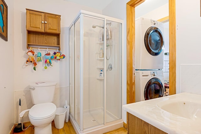 bathroom featuring a stall shower, stacked washer / drying machine, vanity, and toilet