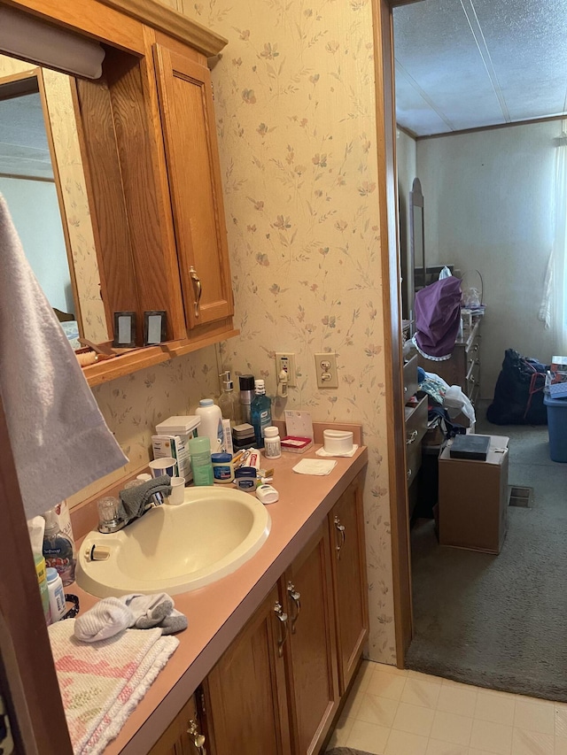 bathroom with a textured ceiling, vanity, and wallpapered walls