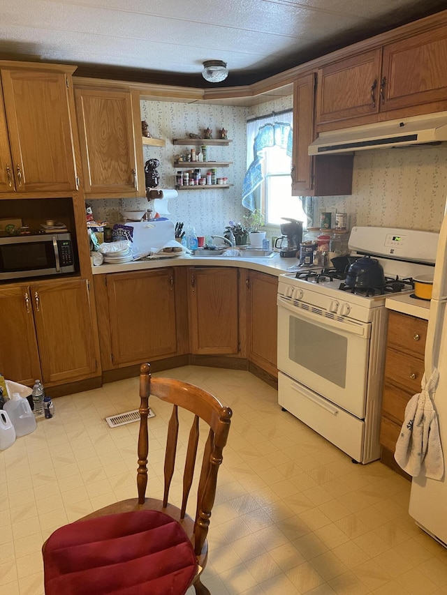 kitchen with stainless steel microwave, light countertops, white gas stove, under cabinet range hood, and a sink