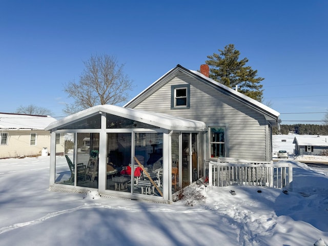 snow covered back of property with a sunroom