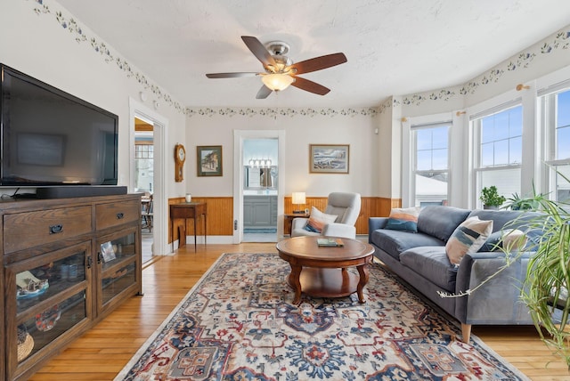 living room featuring ceiling fan, wood walls, light hardwood / wood-style flooring, and a textured ceiling