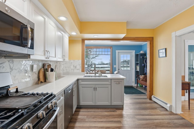 kitchen featuring sink, appliances with stainless steel finishes, hardwood / wood-style floors, decorative backsplash, and a baseboard radiator