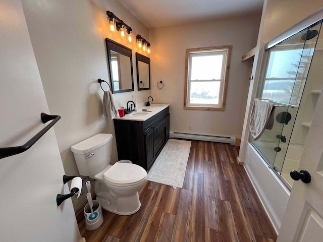 full bathroom featuring toilet, shower / bath combination with glass door, vanity, hardwood / wood-style flooring, and a baseboard heating unit