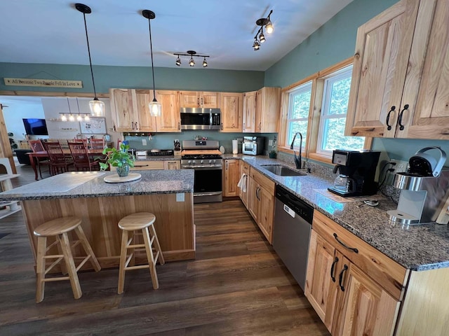 kitchen with a kitchen bar, sink, decorative light fixtures, dark stone countertops, and stainless steel appliances