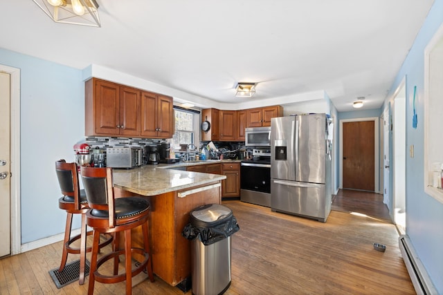 kitchen featuring a breakfast bar area, a baseboard heating unit, hardwood / wood-style flooring, stainless steel appliances, and backsplash